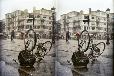 A sudden rainstorm blew a bike over. We are overlooking a wide bridge over a gate in the canal in front of our school. People in the distance walk in the rain. One has a big umbrella.