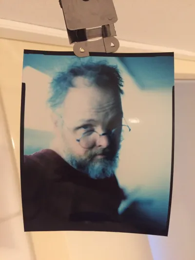 Selfie. Short hair and a beard, myspace angle. The image is both too bright and to dark. Where the background is not washed out, there is a blue color cast.