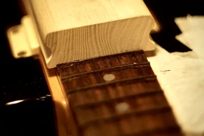 Looking at the bass over the neck. Frets filled with fineer wood. There’s a block of light wood that will later be used to sand the neck. It is in the photo to help with contrast, to make the fineer easy to see.